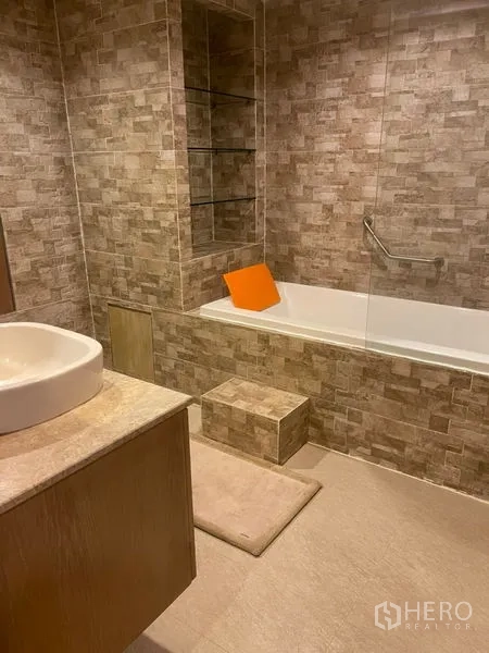 Townhouse for rent in Suan Luang, Bangkok - Contemporary bathroom with stone tiles, built-in shelving, vanity and bathtub with glass screen.