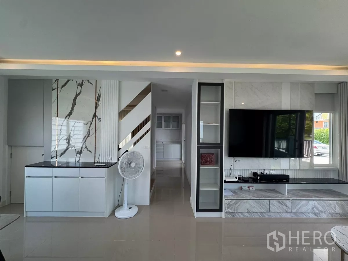 Detached House for rent in Bang Phli, Samut Prakan - Built-in media wall with large flat-screen TV and storage cabinetry looking toward the kitchen.