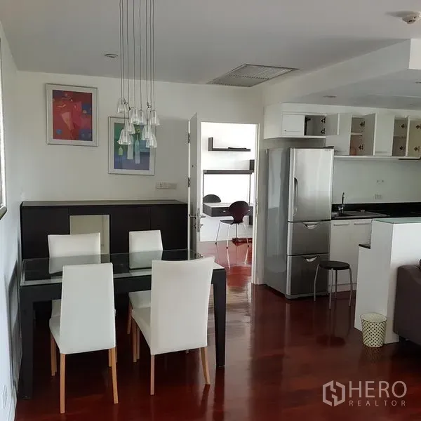 Condominium for rent in Pathum Wan, Bangkok - Dining zone with a glass table and white chairs under pendant lights, next to a modern kitchen and a small study nook.