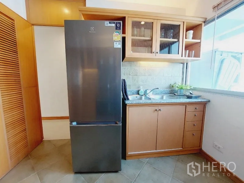 Apartment for rent - Kitchen corner with tall fridge, sink, glass-front cabinets and window light.