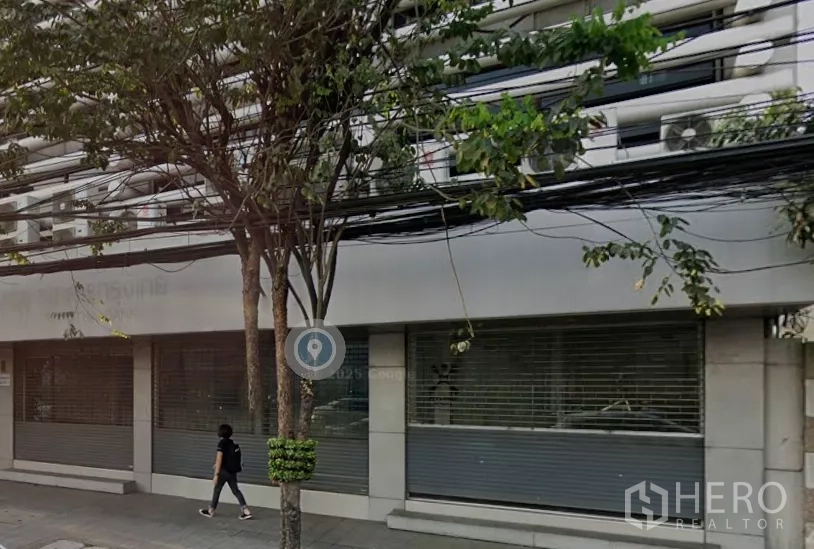 Retail Space for rent in Pathum Wan, Bangkok - Street-level building facade with wide roller shutters, large windows and shaded sidewalk trees.