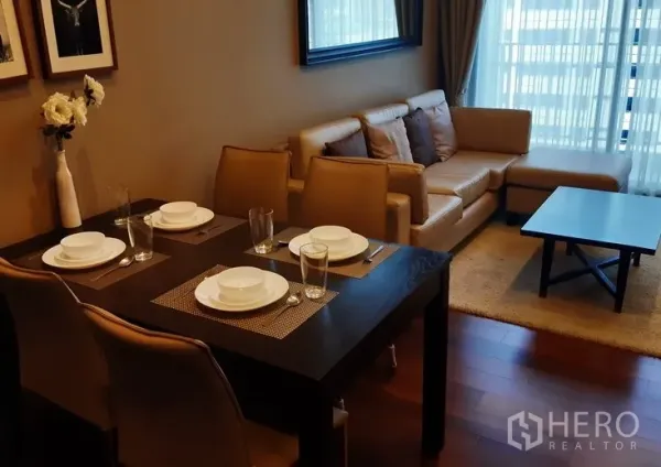 Condominium for rent in Watthana, Bangkok - Open-plan living and dining area with a four-seat table, beige sofa and floor-to-ceiling windows.
