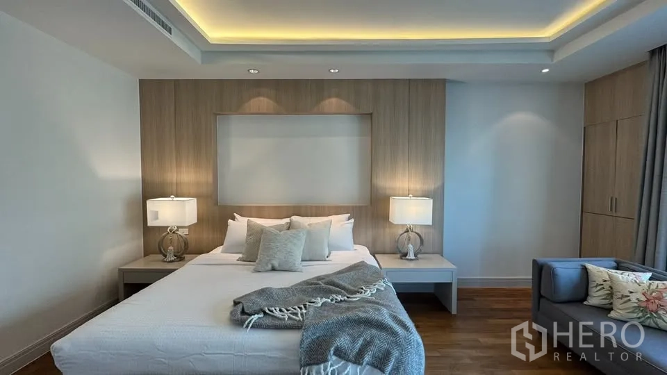 公寓 for rent in Pathum Wan, Bangkok - 主卧配大床与床头灯，木质饰面背景墙、内置衣柜、沙发与灯带吊顶。