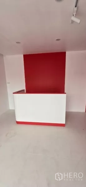 พื้นที่ขายของ for rent in Watthana, Bangkok - ภายในร้านค้าขนาดกะทัดรัด ผนังแต่งสีแดง เคาน์เตอร์ต้อนรับสีขาว และไฟดาวน์ไลท์