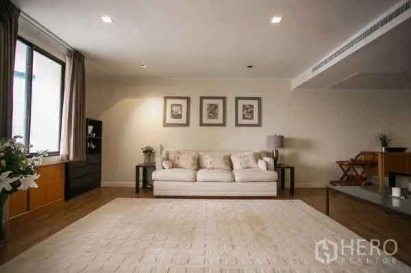Condominium for rent or sale in Watthana, Bangkok - Bright living room with cream sofa, large rug and wall art on warm wood floors.