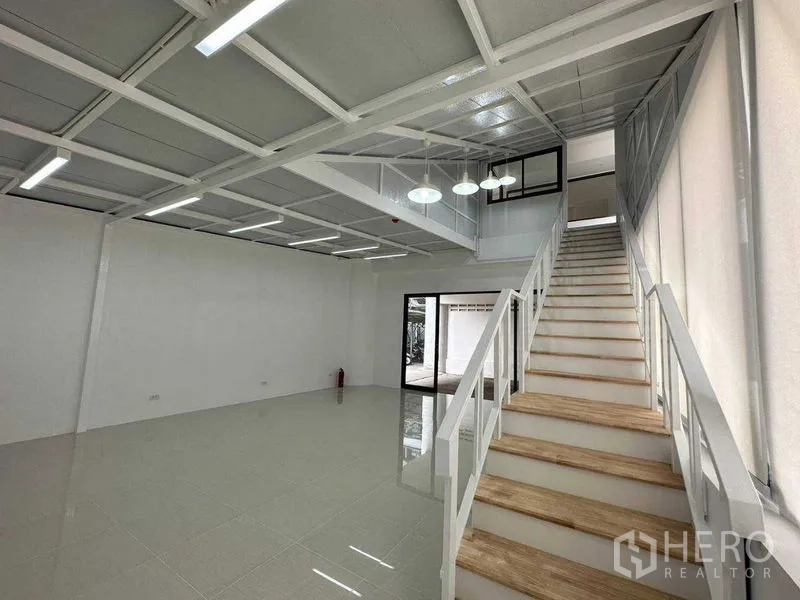 Office Space for rent or sale in Khlong Toei, Bangkok - Spacious double-height workspace with staircase and hanging pendant lights.