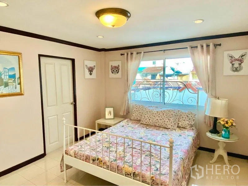 联排别墅 出租或出售在Prawet, Bangkok - 温馨卧室，双人床、阳台窗、床头柜与窗帘。