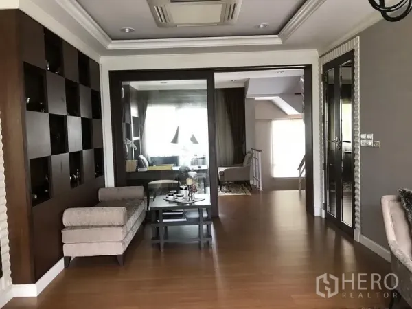 Townhouse for rent or sale in Bang Kho Laem, Bangkok - Upper-floor family room with wood flooring, built-in shelving and glass doors leading to another sitting area and stairs.