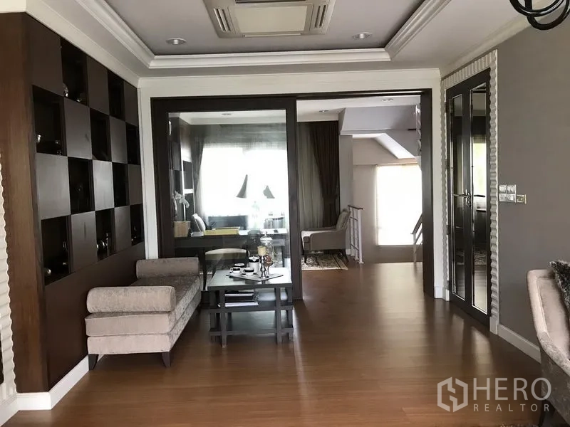 Townhouse for rent or sale in Bang Kho Laem, Bangkok - Upper-floor family room with wood flooring, built-in shelving and glass doors leading to another sitting area and stairs.