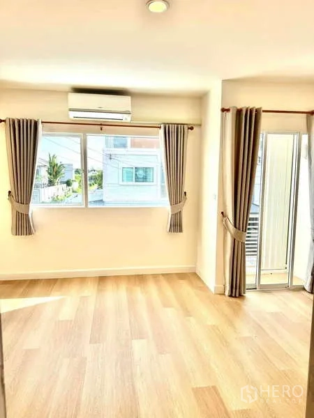 Townhouse for rent in Suan Luang, Bangkok - Sunlit bedroom featuring corner windows, curtains, air-conditioning, and a balcony door.