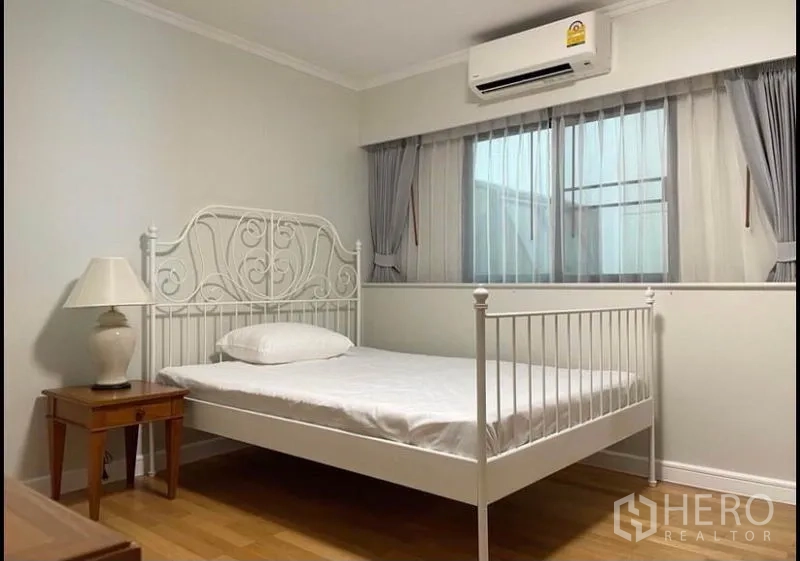 Condominium for rent in Sathon, Bangkok - Cozy bedroom with white metal bed frame, curtains and an air conditioner.