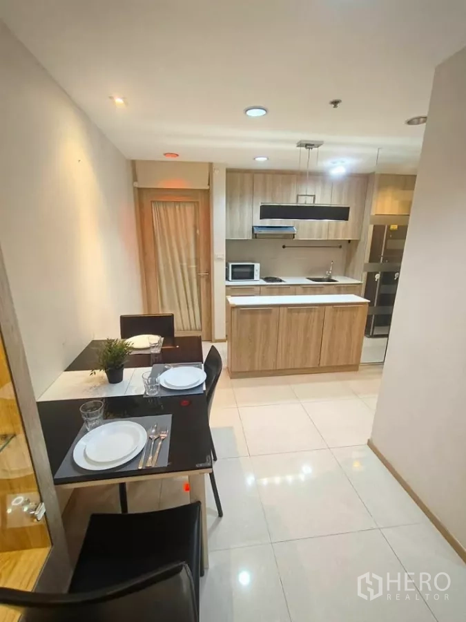 Condominium for rent in Khlong Toei, Bangkok - Dining table for four next to a compact kitchen with a wooden island on glossy tiled floors.