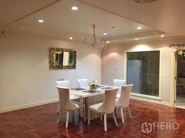 公寓 出租在Watthana, Bangkok - 餐区配六人餐桌与水晶吊灯，旁边是通向厨房的玻璃窗。