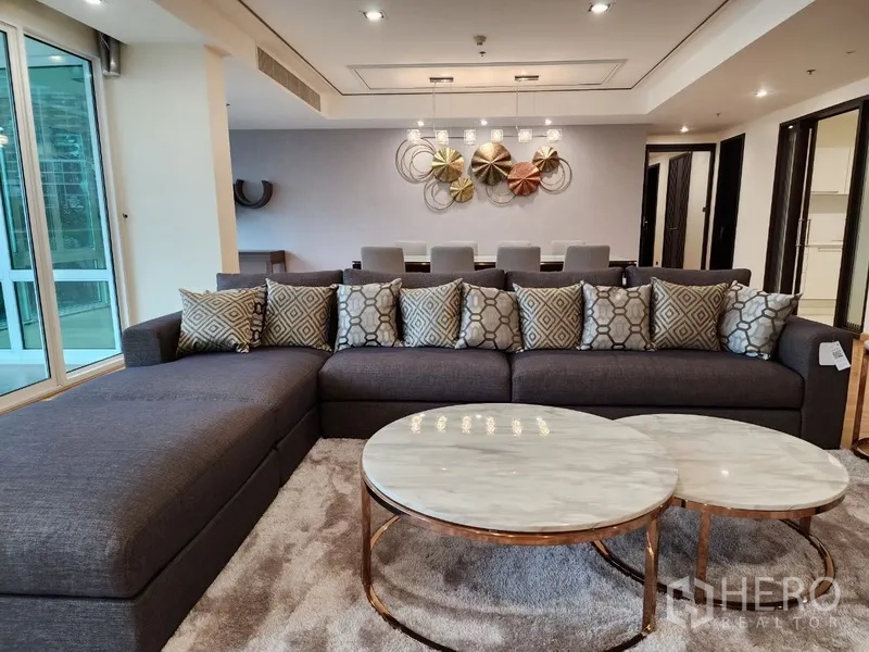 Condominium for rent in Khlong Toei, Bangkok - Lounge area with sectional sofa and marble coffee tables facing dining zone.