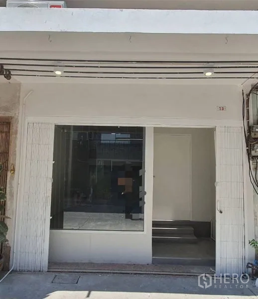 Shophouse for rent in Phra Khanong, Bangkok - Clean white shopfront with large display window and recessed doorway at ground level.