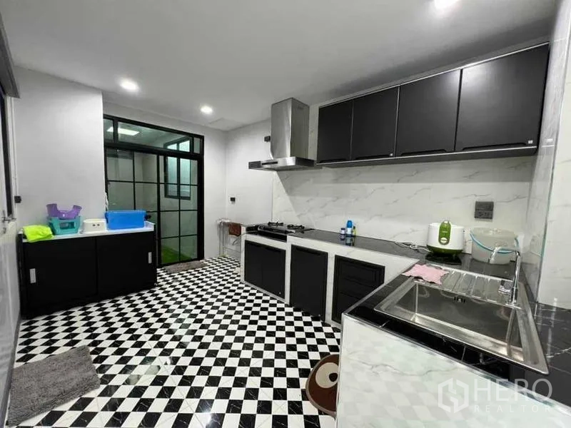 Detached House for sale in Khan Na Yao, Bangkok - Spacious kitchen with black cabinets, marble-look wall, range hood and checkered floor tiles.