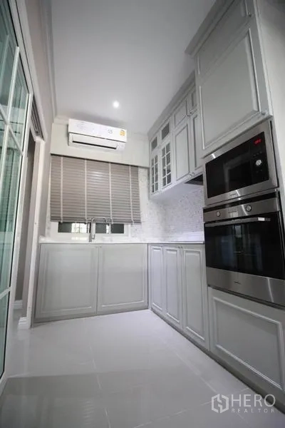 Detached House for rent or sale in Lat Phrao, Bangkok - Galley kitchen with white cabinetry, stone backsplash, sink beneath window and built-in oven.