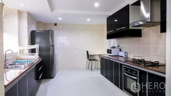 Condominium for rent or sale in Khlong Toei, Bangkok - Fully fitted kitchen with black cabinetry, gas hob, oven, hood and large fridge.