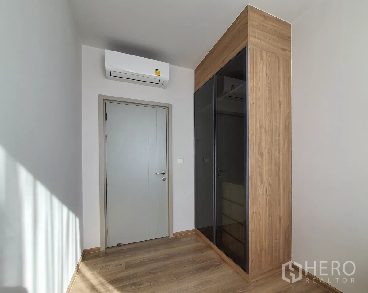 Condominium for rent in Khlong Toei, Bangkok - Empty room with wood floors, built‑in wardrobe and air conditioner.