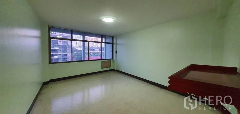 Warehouse for rent in Bang Kho Laem, Bangkok - Empty office room with large windows, pale green walls, and city view.