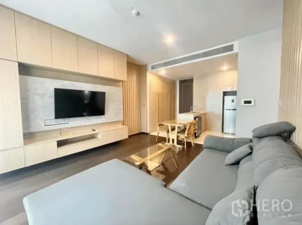 公寓 出租在Watthana, Bangkok - 现代客厅，灰色转角沙发、电视墙，与开放式厨房相连。