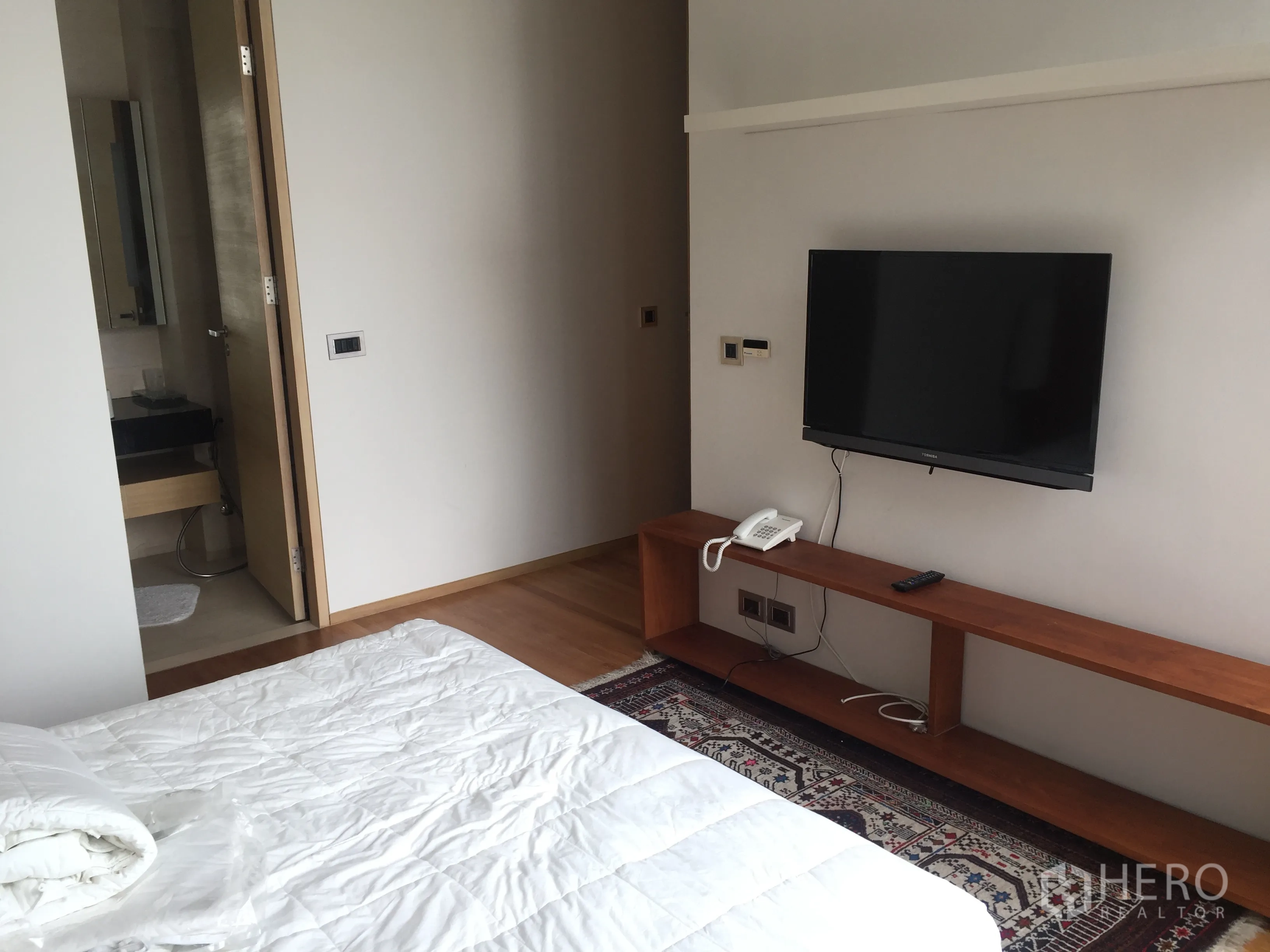 Condominium for rent in Bang Rak, Bangkok - Bedroom with wall-mounted TV, long wooden console and doorway to an ensuite bathroom.