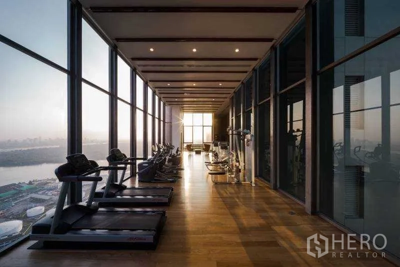 公寓 出租或出售在Bang Rak, Bangkok - 高层健身房，跑步机面向落地玻璃，可俯瞰河景与城市天际线。