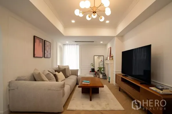 Condominium for sale in Watthana, Bangkok - Bright living room in Watthana condo with plush sectional, wood media console and modern chandelier.
