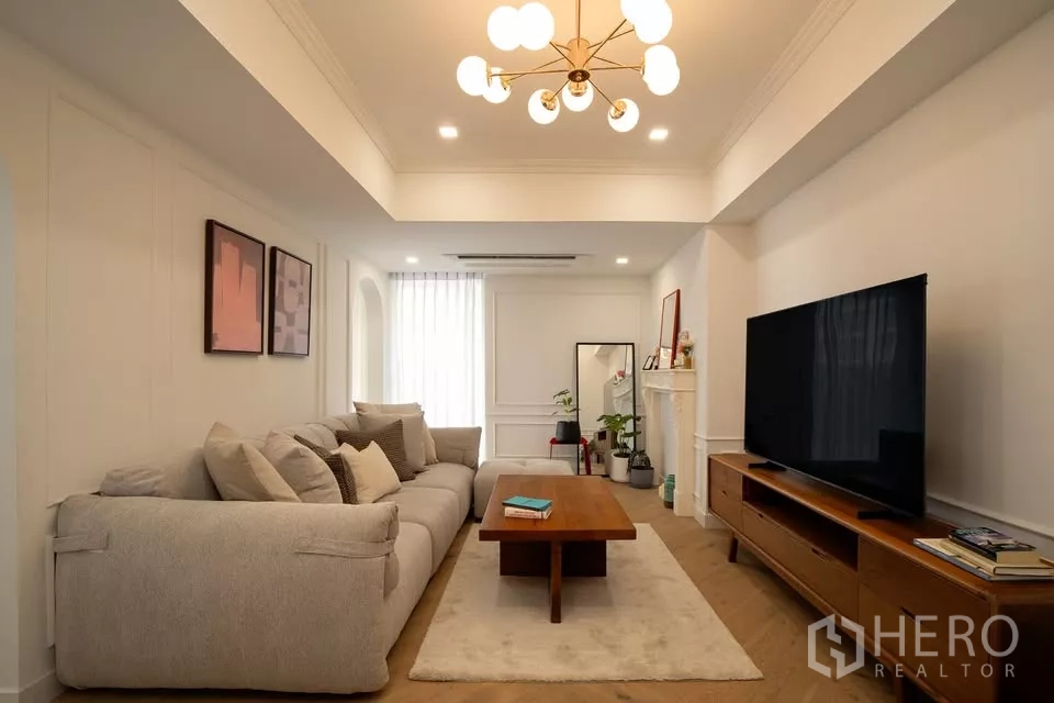 Condominium for sale in Watthana, Bangkok - Bright living room in Watthana condo with plush sectional, wood media console and modern chandelier.
