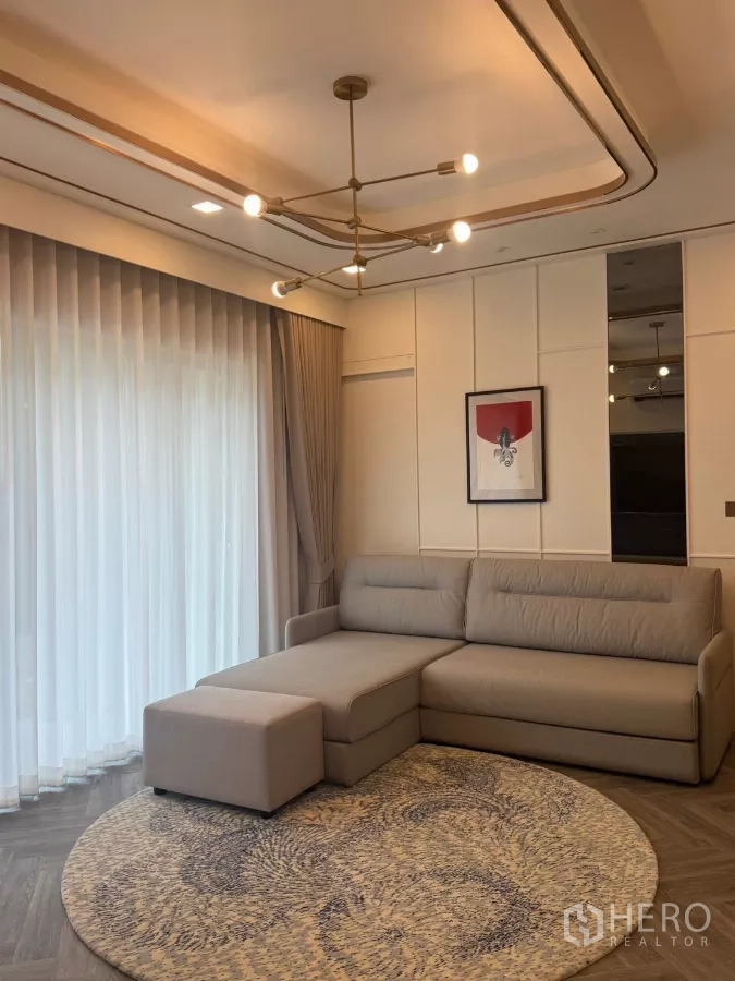 Detached House for rent in Lat Krabang, Bangkok - Living room with sectional sofa, round rug and contemporary chandelier near full-height curtains.