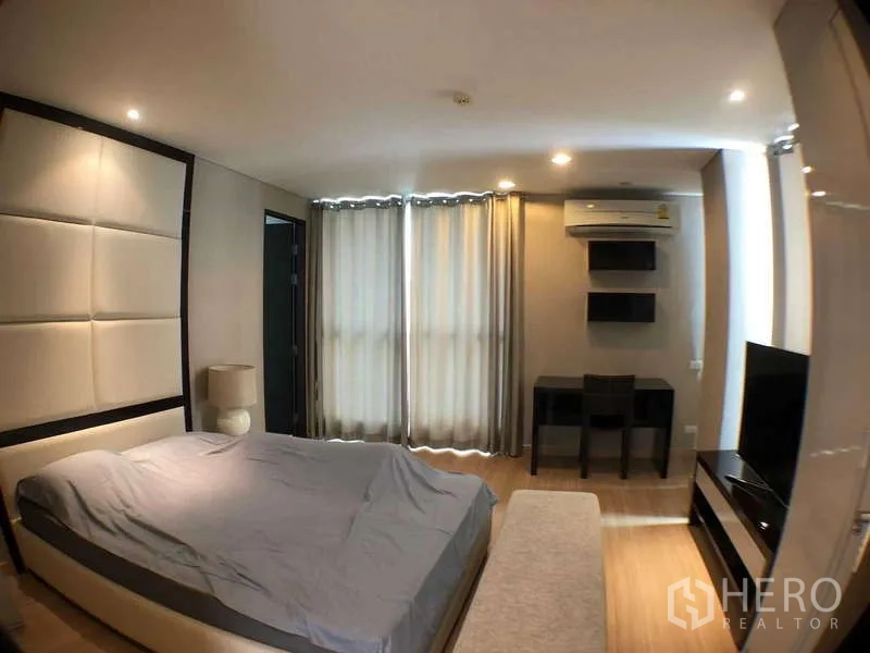 คอนโด ให้เช่าในRatchathewi, Bangkok - ห้องนอนหลักมีหัวเตียงบุผ้า โต๊ะทำงาน ชั้นวางทีวี และผ้าม่านสูงจรดเพดาน
