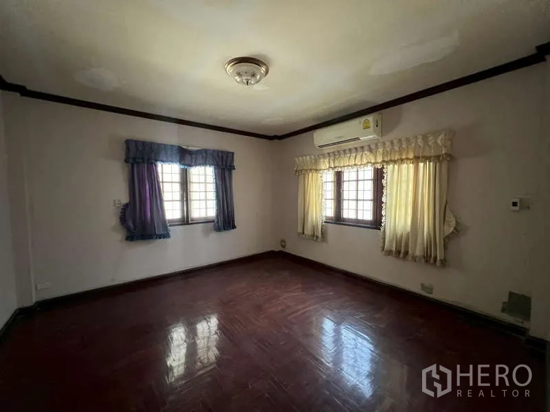 Detached House for rent in Prawet, Bangkok - Bedroom with wood floor, air conditioner and two curtained windows.