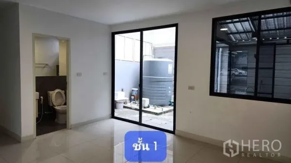 Townhouse for rent in Bueng Kum, Bangkok - Ground-floor multipurpose room with bathroom and sliding glass door opening to a utility yard with water tank.
