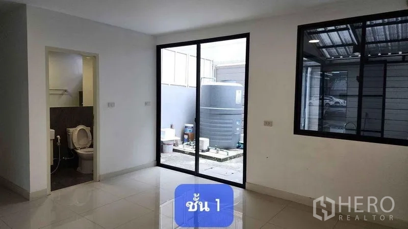 Townhouse for rent in Bueng Kum, Bangkok - Ground-floor multipurpose room with bathroom and sliding glass door opening to a utility yard with water tank.