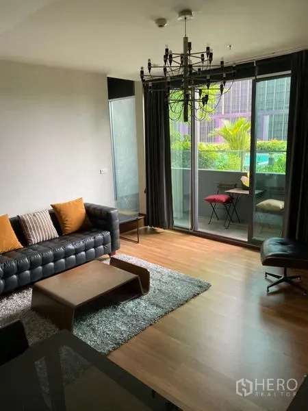 Condominium for rent in Khlong Toei, Bangkok - Bright living room with floor-to-ceiling sliding doors to a balcony, pool and garden view, leather sofa and curtains.