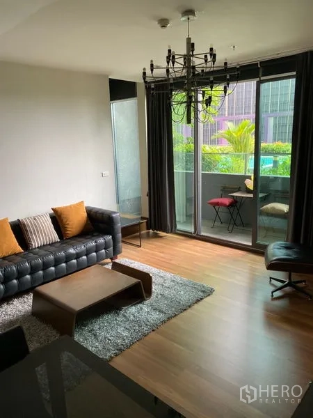 Condominium for rent in Khlong Toei, Bangkok - Bright living room with floor-to-ceiling sliding doors to a balcony, pool and garden view, leather sofa and curtains.