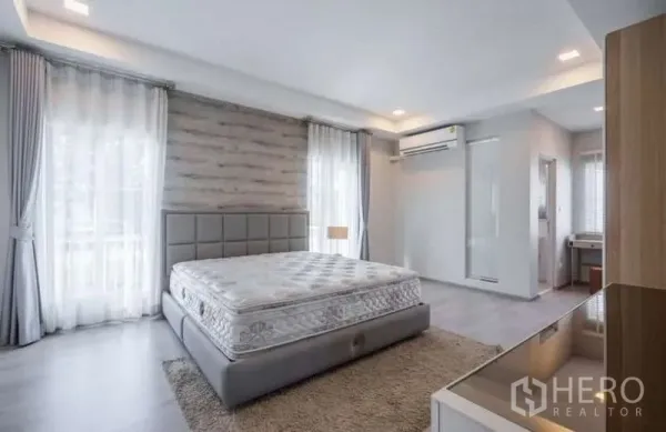 独立式住宅 出租在Prawet, Bangkok - 明亮主卧，落地窗、软包大床、空调与木质特色墙。