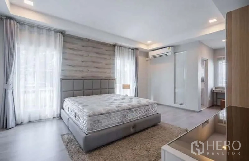 独立式住宅 出租在Prawet, Bangkok - 明亮主卧，落地窗、软包大床、空调与木质特色墙。