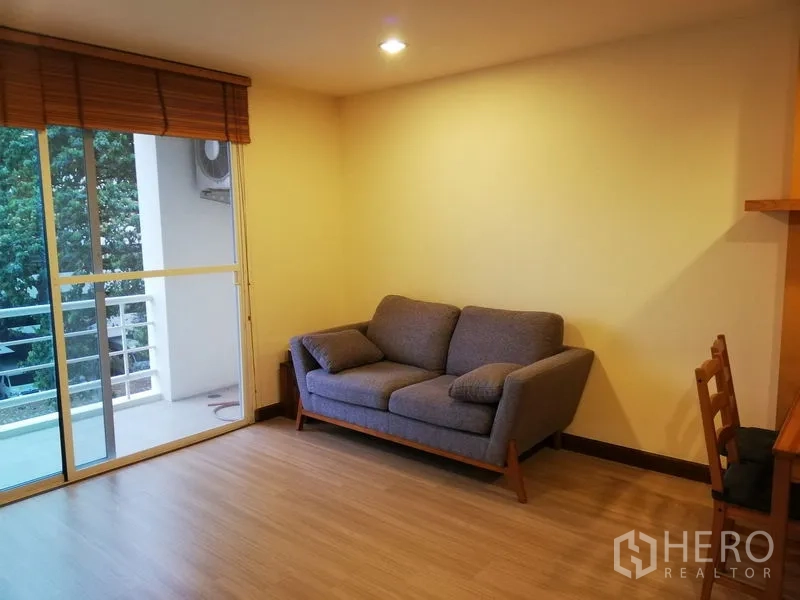 公寓 出租在Watthana, Bangkok - 温馨客厅配灰色沙发，通向阳台，可观赏绿景。
