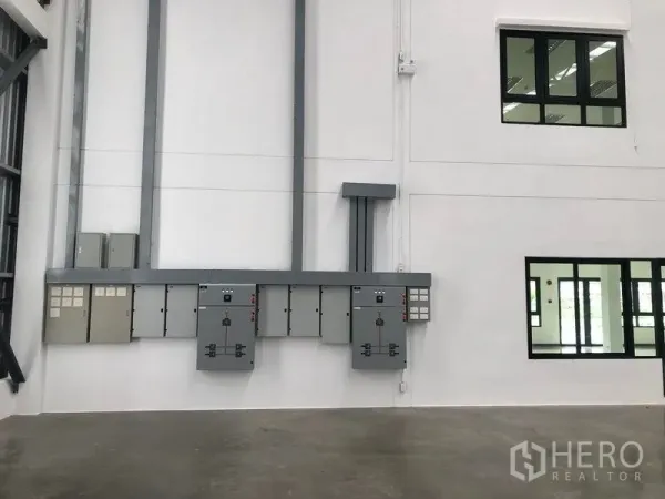 Factory for rent in Wang Noi, Phra Nakhon Si Ayutthaya - Electrical control panels mounted on a white wall beside internal office windows in the factory.