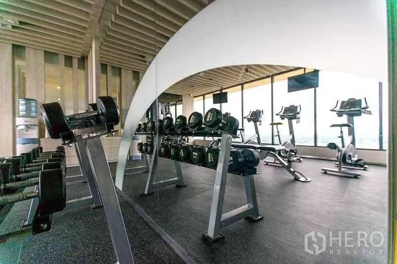 Condominium for rent in Khlong Toei, Bangkok - Fitness center with free weights and cardio machines beside panoramic windows.