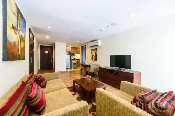 Condominium for rent in Khlong Toei, Bangkok - Bright living room with beige sofas, TV console, wood floors and open-plan layout leading to the kitchen.