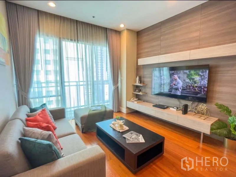 Condominium for rent in Khlong Toei, Bangkok - Living area with floor-to-ceiling windows, sheer curtains, sofa and floating TV console.