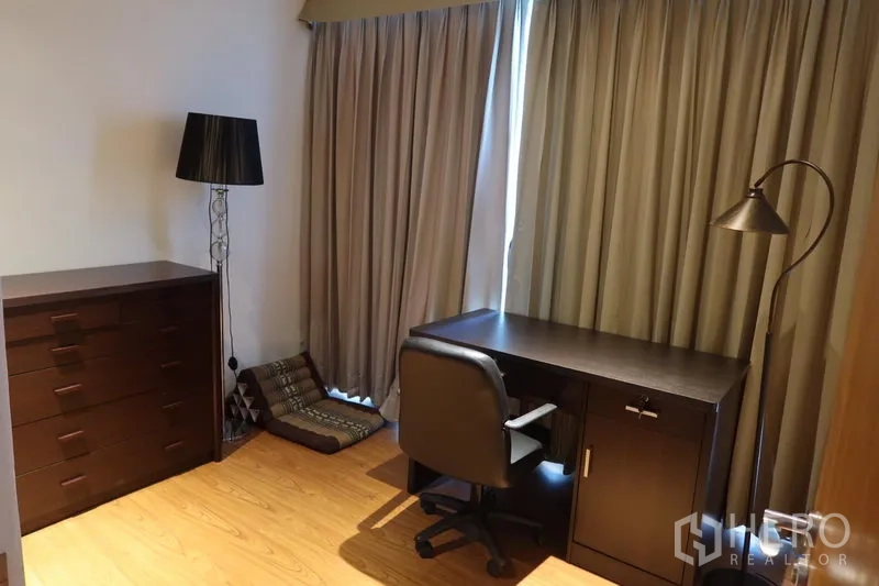 Condominium for rent in Khlong Toei, Bangkok - Quiet study or second bedroom with dark wood desk, office chair, dresser and floor lamp.