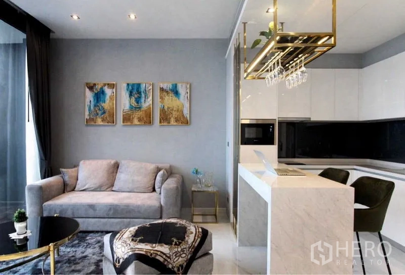 Condominium for rent in Bangkok - Open-plan kitchen with marble breakfast bar, hanging rack and grey sofa seating.