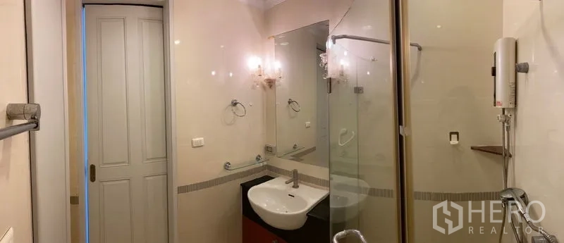 Condominium for rent in Ratchathewi, Bangkok - Modern bathroom with glass-enclosed shower, vanity basin, and wall mirror.