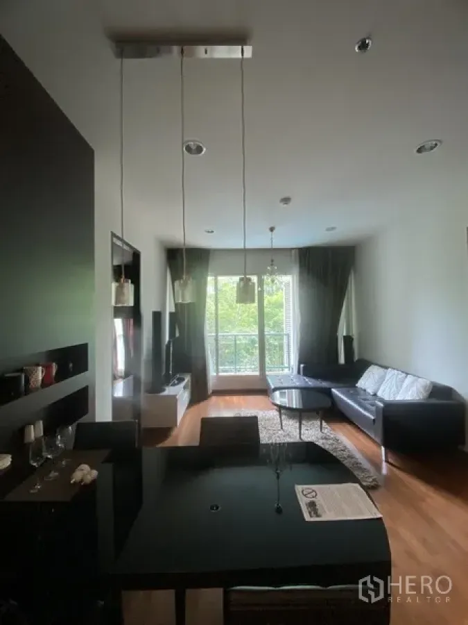 公寓 出租在Pathum Wan, Bangkok - 开放式客餐厅，黑色餐桌、沙发、电视柜，木地板，落地窗与阳台望向绿意。