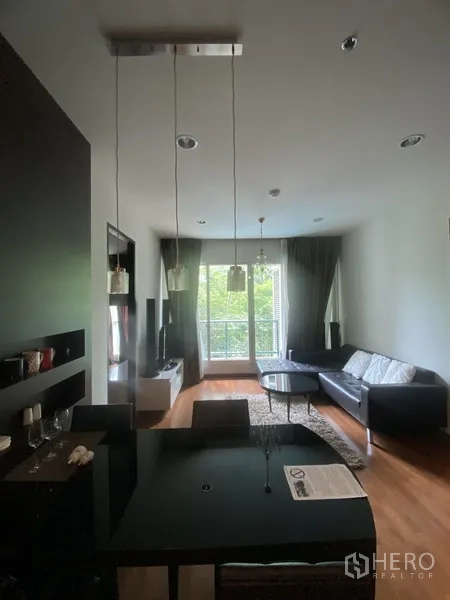 公寓 出租在Pathum Wan, Bangkok - 开放式客餐厅，黑色餐桌、沙发、电视柜，木地板，落地窗与阳台望向绿意。