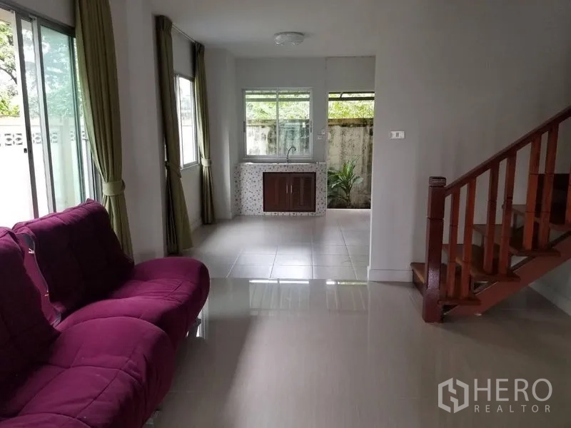 Townhouse for rent in Bang Kapi, Bangkok - Bright living room with purple sofa, tiled floors, large windows and a wooden staircase.