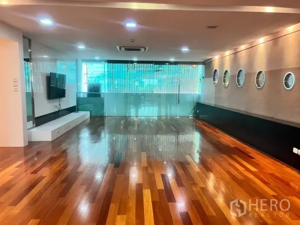 Condominium for rent in Khlong Toei, Bangkok - Spacious living room with glossy hardwood floors, recessed lights, TV wall and a glass partition.